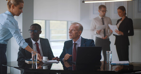 Secretary bring coffee to diverse business partners discussing contract on laptop