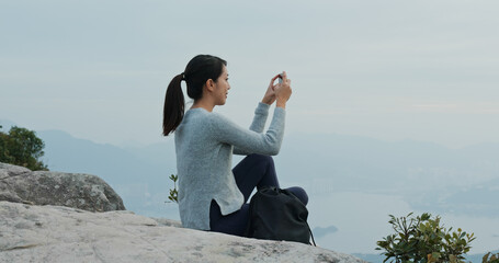 Poster - Woman sit on the rock and use cellphone to take photo on mountain