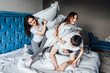 © Тарас Нагирняк - Cute smiling family fighting with pillows on bed in bedroom.