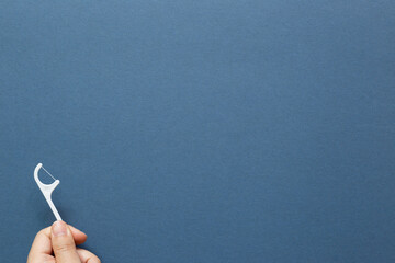 Hand holding a white dental floss stick on navy blue background. top view, copy space