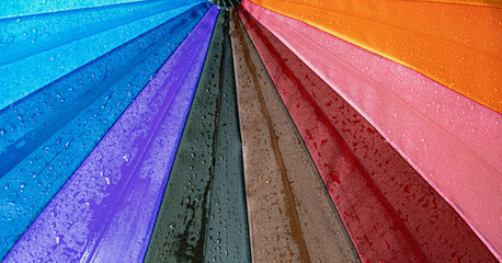 wet waterproof textile surface of rainbow colored umbrella under drizzle rain. water drops dripping 