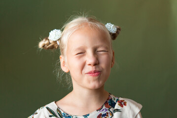 Beautiful blonde girl with a hairstyle in the form of two horns on an olive green background. Great for demonstrating the character of a child - daydreaming, enthusiasm, vulnerability, stubbornness.