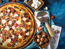 A Beautiful Composition In Which We See A Large Round Pizza, Mushrooms, Eggs In Wooden Bowls, And A Pizza Knife. Dark Blue Background. High Angle View.