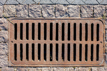 Wall Mural - rusty manhole rectangular grating of the drainage system of the pedestrian sidewalk from rough cut stone tiles top view.