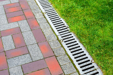 Wall Mural - iron grating line of the drainage system of the pedestrian sidewalk made of stone tiles landscaping of the park with engineering systems on side of the path with the green lawn of the park, nobody.