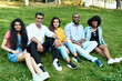 © etonastenka - Multi-ethnic friends are sitting on the grass in the park and looking at the camera, smiling