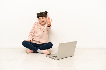 Little girl with a laptop sitting on the floor happy and counting four with fingers