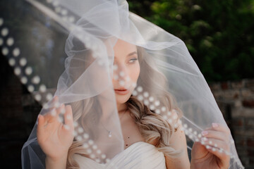 happy bride with long wavy hair under the veil outside. Wedding make-up. 