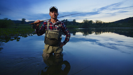 Wall Mural - Fly fisherman stands on the river and looks into the camera