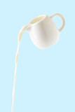 Fototapeta Na ścianę - pouring milk from milk jug isolated on blue background