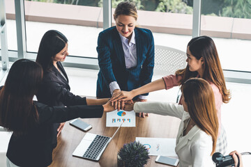 Businesswomen joining hands in group meeting at modern office room showing teamwork, support and unity in work and business. Female power and femininity concept.