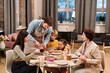 © pressmaster - Young man pouring black tea into cup of his wife among family gathered by served table