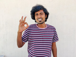 Wall Mural - Smiling Young handsome man without beard wearing casual tshirt over white background doing ok sign with hand and fingers. Successful.