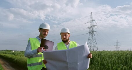 Wall Mural - two engineers look at drawings in an unfolded paper poster against the background of a high-voltage 