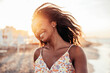 © Davide Angelini - Cheerful woman smiling at the beach on sunset  - Happy african female having fun walking by the sea - People and happiness concept