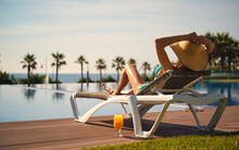Rear View Woman Wear Hat Sunbathing On Deckchair On Poolside