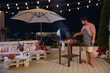 a man grilling barbecue on rooftop patio, enjoys warm summer night at home courtyard