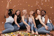 © Artem Varnitsin - Group of happy women sitting on the brown background while petals from flowers falling. Laughing females of different races and ages under petals from flowers.
