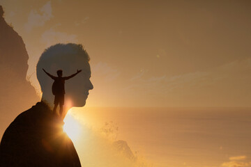 silhouette of a man climbing to the top of a mountain with arms up to the sky. young man looking to 