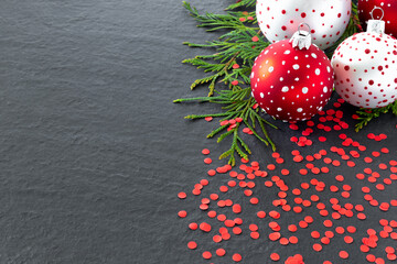 Wall Mural - Three  red and white Christmas toy balls, holiday confetti and christmas tree branches on black background.