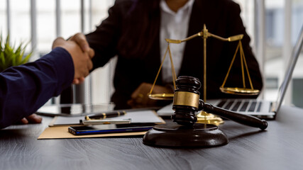 Lawyers shake hands with clients to work on contract documents and hammer with scales and laptops on a courtroom table. Judiciary concept