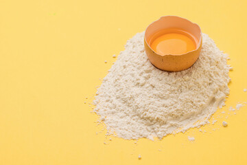 Half a raw egg on a pile of flour on a yellow background.