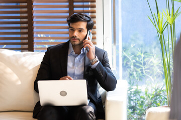 young hispanic businessman working on laptop computer and talking on mobile phone.