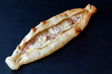 Wall Mural - Closeup of an appetizing pide flatbread stuffed with ham and cheese topping on a dark surface