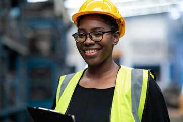 Plus size black female worker wearing safety hard hat helmet inspecting old car parts stock while working in automobile large warehouse