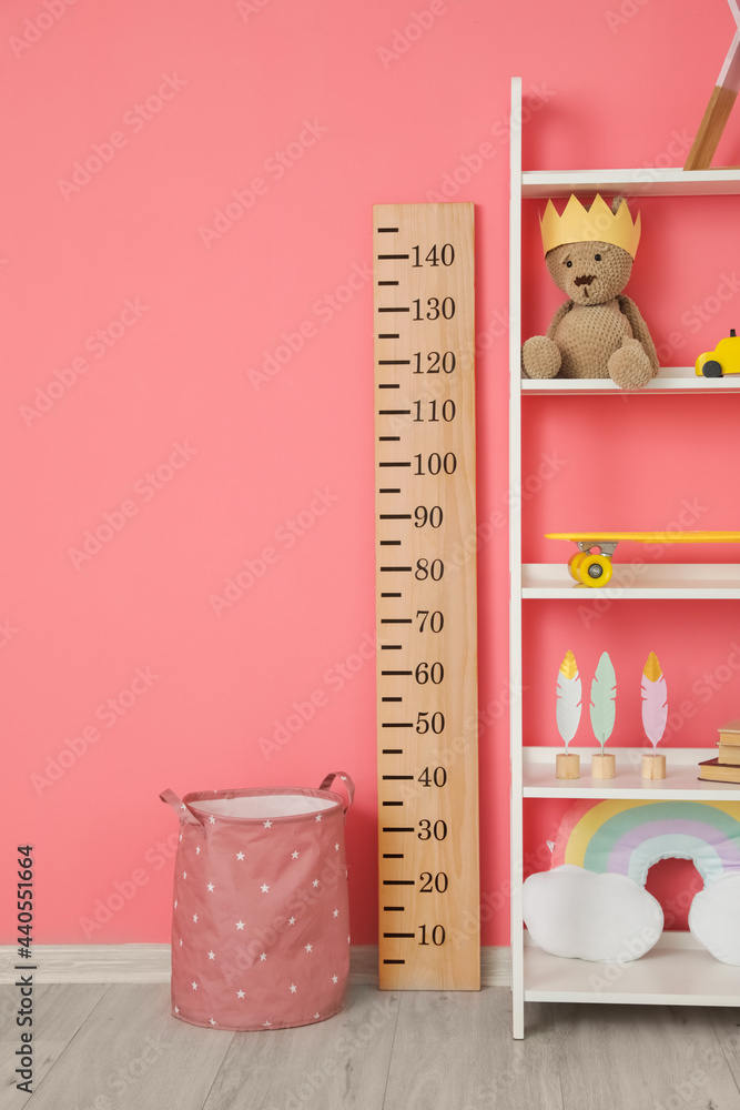 Modern shelf with toys and stadiometer near color wall