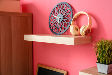 Modern headphones with clock on shelf in room