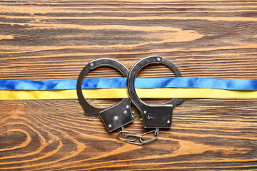 Handcuffs with ribbons in colors of Ukrainian flag on wooden background