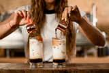 process of making macchiato with syrup. Woman pours coffee from cups into glasses