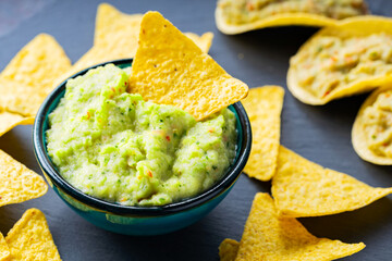 Wall Mural - Guacamole and nachos chips on a dark background. Guacamole sauce with corn chips on a slate board. Close-up. Selective focus