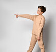 Serious thoughtful confident young boy in sports fashion shows his finger at copy space. sideways on studio wall background. Children emotion and expression concept