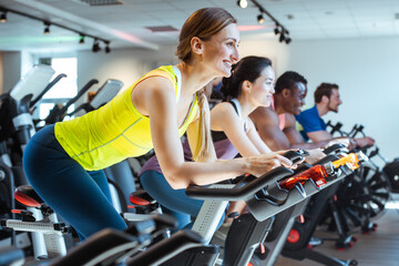 Very fit Caucasian woman and her friends on fitness bike in gym