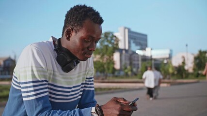 A young black student in stylish clothes sits and talks on a smartphone in the city