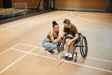 High Angle View At Young Woman In Wheelchair Talking To Female Coach During Badminton Practice At Sports Court And Using Smartphone, Copy Space