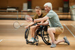 Full length portrait of mature coach training young woman in wheelchair at badminton practice in sports court, copy space