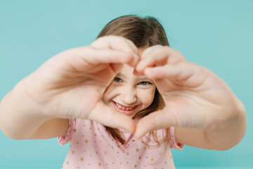 Close up little fun kid girl 5-6 years old wears pink dress show look through shape heart with hands isolated on pastel blue color background child studio. Mother's Day love family lifestyle concept.