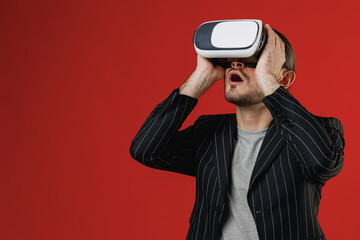 Wall Mural - Young excited shocked impressed happy joyful amazed fun unshaven latin man 20s wear black striped jacket grey shirt watching in vr headset pc gadget isolated on red color background studio portrait