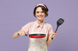 Young smiling happy fun cheerful housewife housekeeper chef cook baker woman in pink apron hold show red frying pan spatula isolated on pastel violet background studio Cooking food process concept