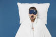 Young happy fun caucasian man 20s wearing pajamas jam sleep mask resting relaxing at home lies wrap covered under blanket duvet yawn isolated on dark blue background. Good mood night bedtime concept.