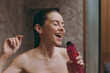 © ViDi Studio - Half naked topless fun young wet haired woman 20s take hot shower sing song in bottle microphone in bathroom do morning routine in brown background. Skin care healthcare cosmetic procedures concept