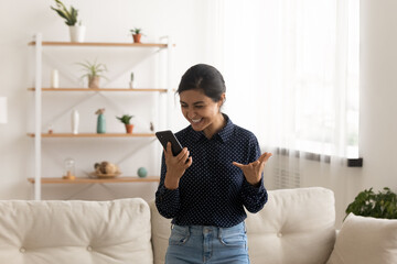 Wall Mural - Excited young Indian woman look at cellphone screen feel euphoric with online lottery win or victory. Happy millennial mixed race female triumph with good news or promotion letter on smartphone.