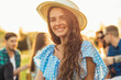 Happy young woman in a summer hat and dress, spends time together with her friends, on a picnic in the park, sitting on the lawn