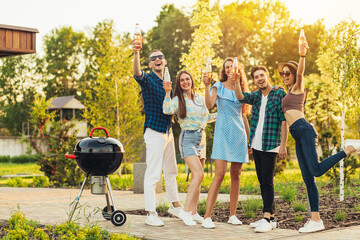 Wall Mural - Group of young friends standing around outdoor barbecue grill, celebrate drinking cocktails and having fun in the park