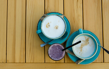 Two cups of cappuccino in blue cups, glass cup with blackberry mousse on wooden table