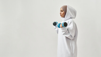 Wall Mural - Cute young arabian woman in hijab holding dumbbells