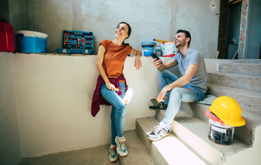 Modern happy young couple in love in casual clothes during new home repair or renovation of walls with a lot of tools for this